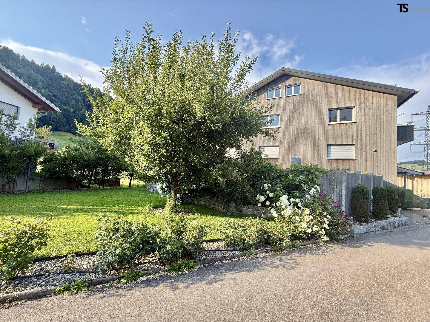 Haus mit Holzfassade in ländlicher Umgebung, umgeben von Grünflächen und mit Bergblick.
