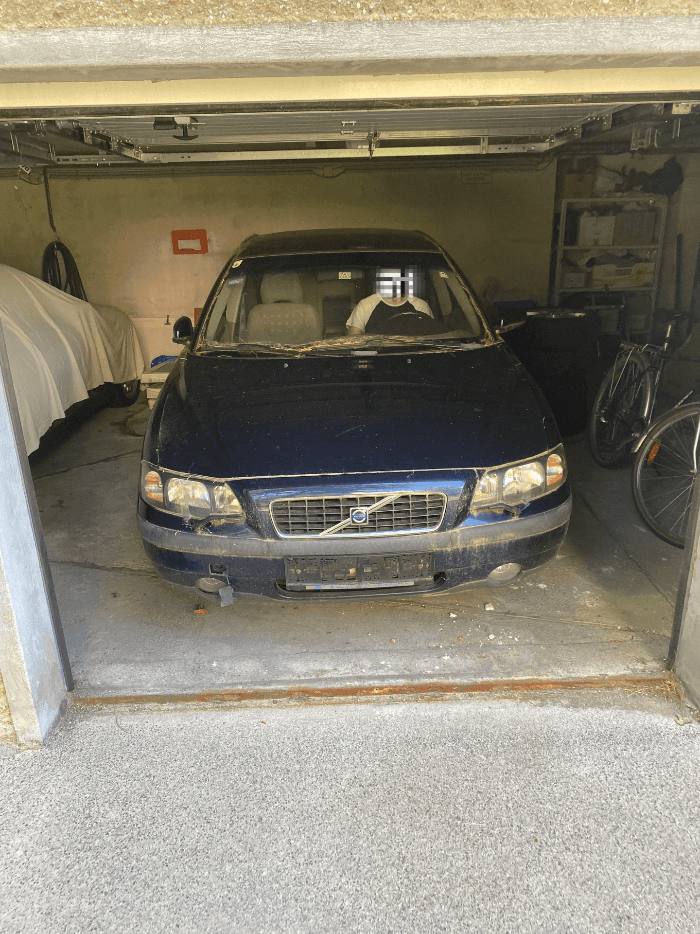 Geräumige Garage mit einem geparkten Auto, Stauraum und einem Fahrrad, gut beleuchtet durch Tageslicht.