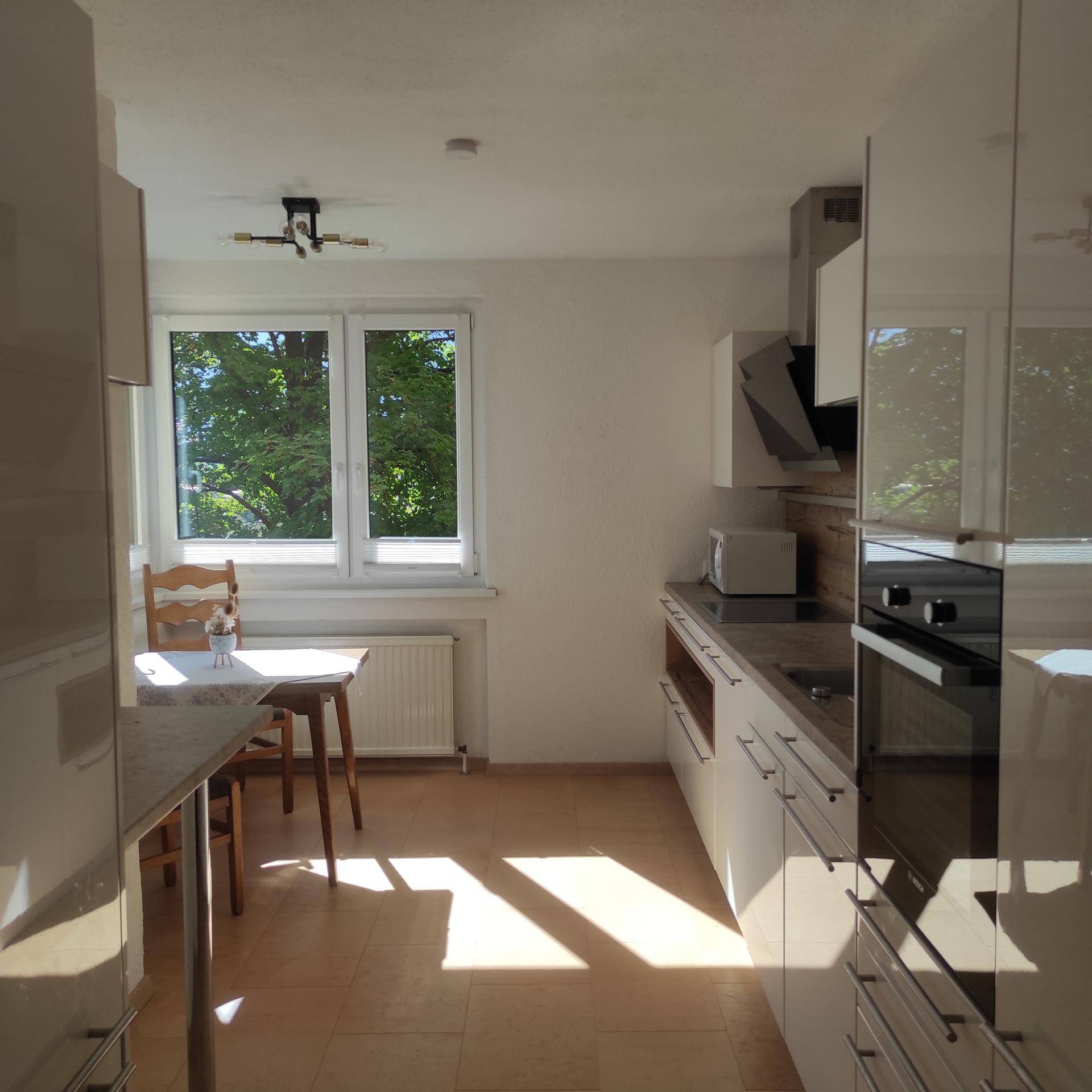 Helle, moderne Küche mit weißen Hochglanzfronten, Essbereich am Fenster und viel Tageslicht.