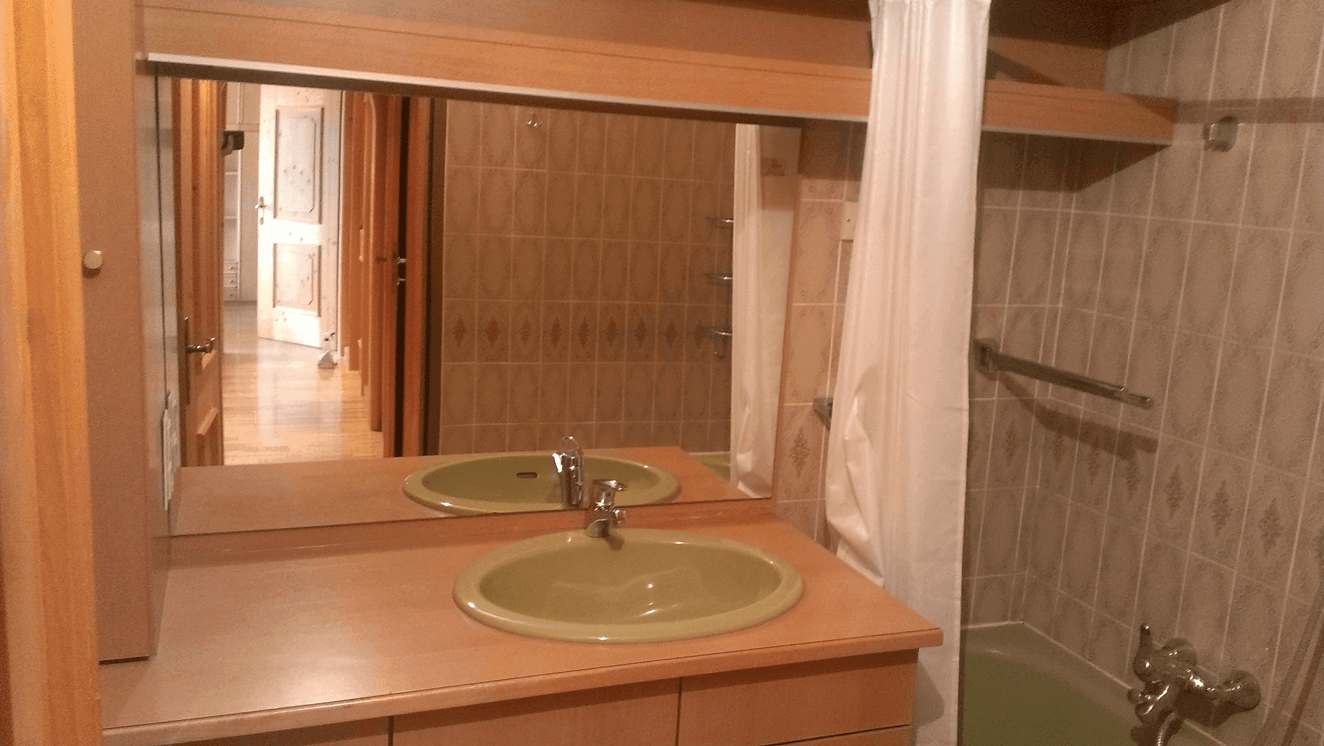 Badezimmer mit großem Spiegel, grünem Waschbecken und Badewanne mit Duschvorhang.