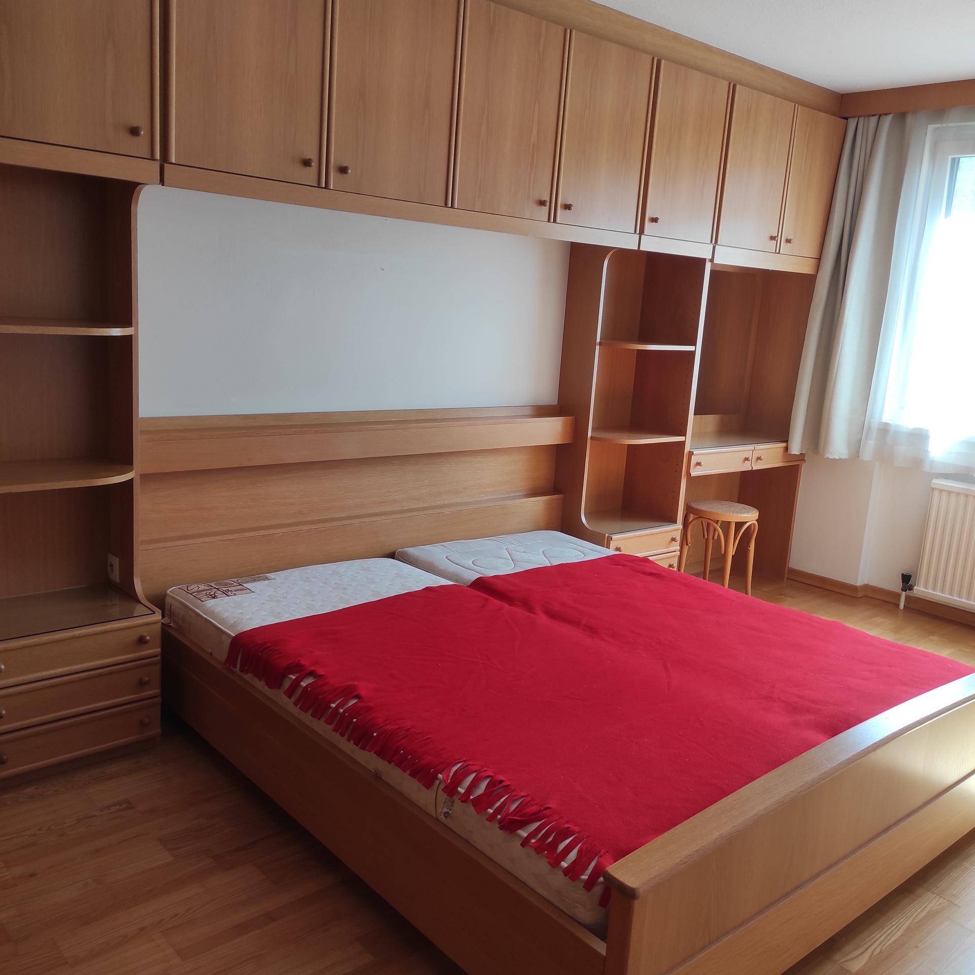Schlafzimmer mit großem Bett und praktischen, integrierten Holzschränken und Regalen für Stauraum.