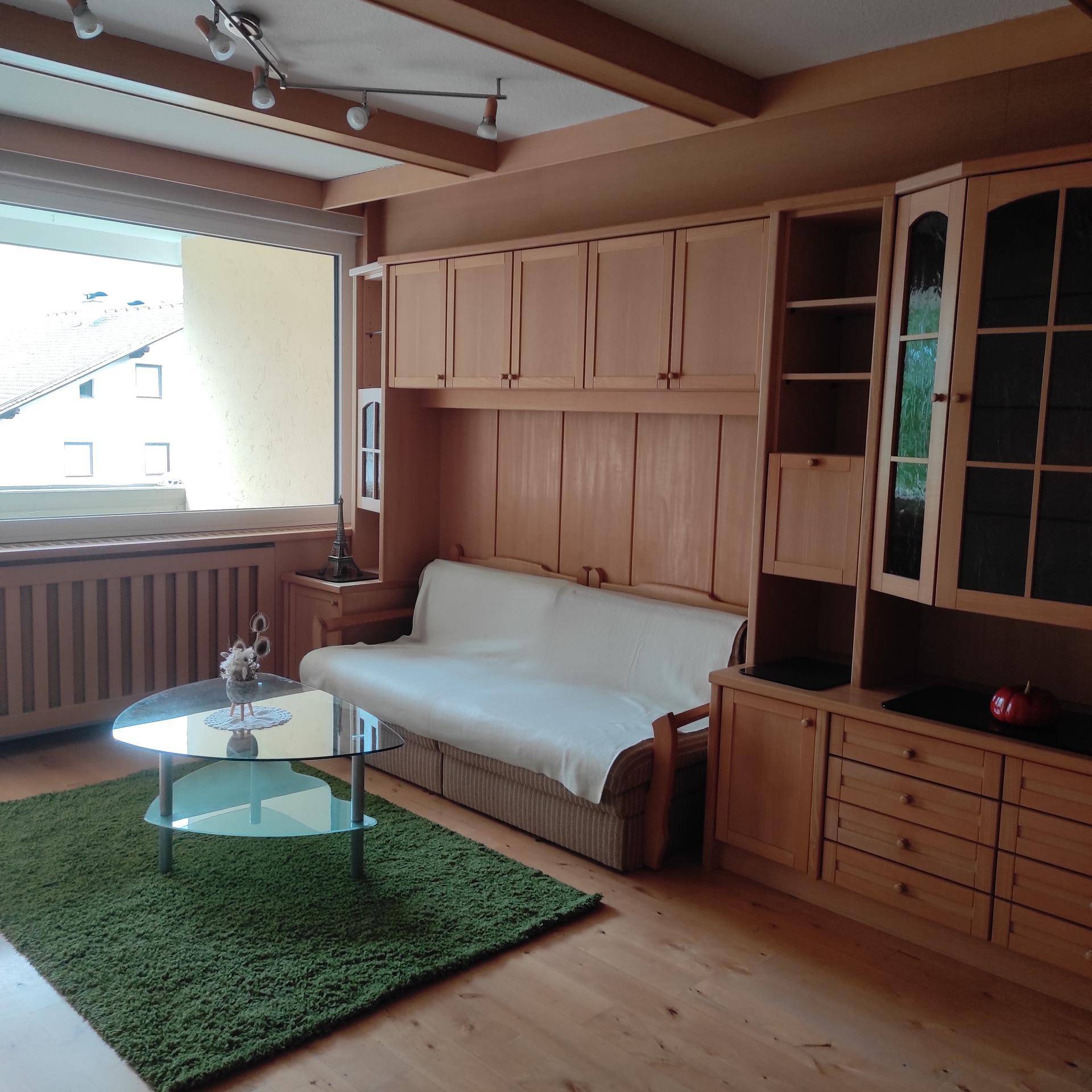 Gemütliches Wohnzimmer mit Schlafsofa, Holzmöbeln, einem Glastisch und Blick auf die Umgebung.