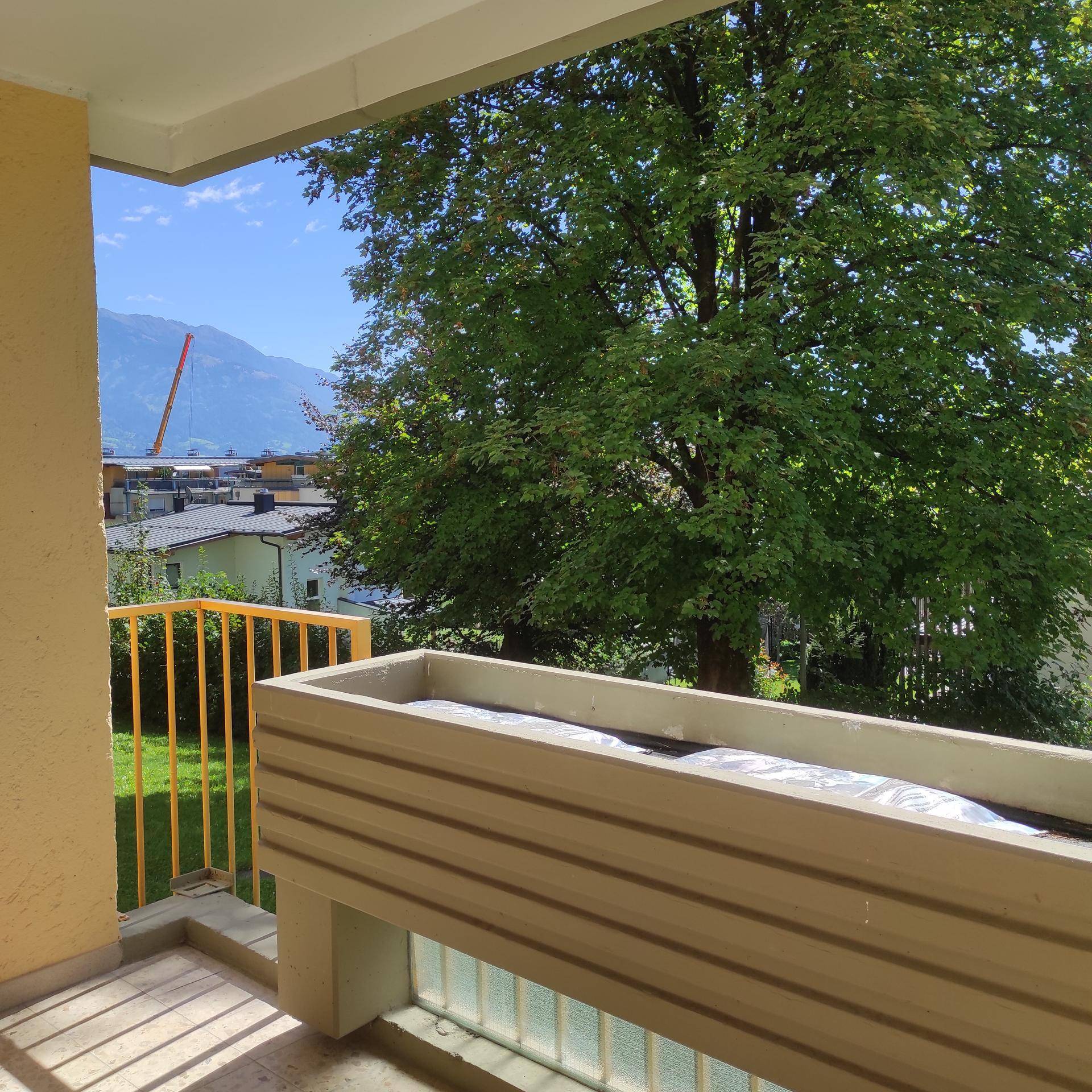 Balkon mit Blumenkasten, Blick auf grüne Bäume und die umliegende Berglandschaft.