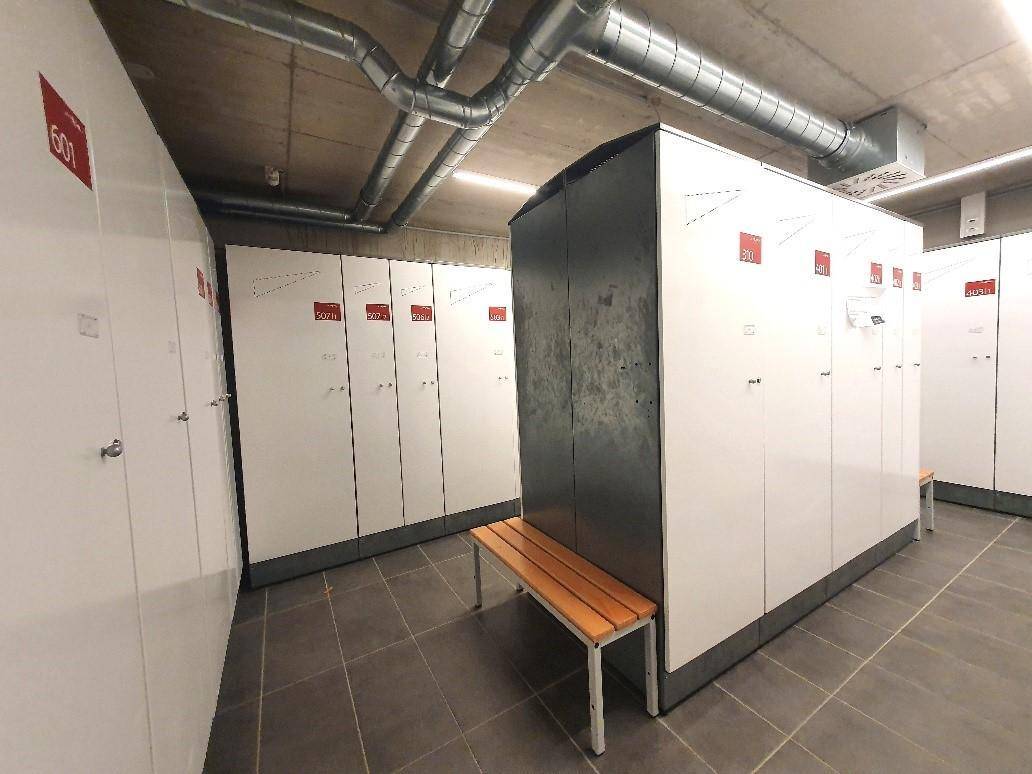 Praktischer Abstellraum mit weißen Schließfächern und einer Sitzbank, ideal für Sportausrüstung.