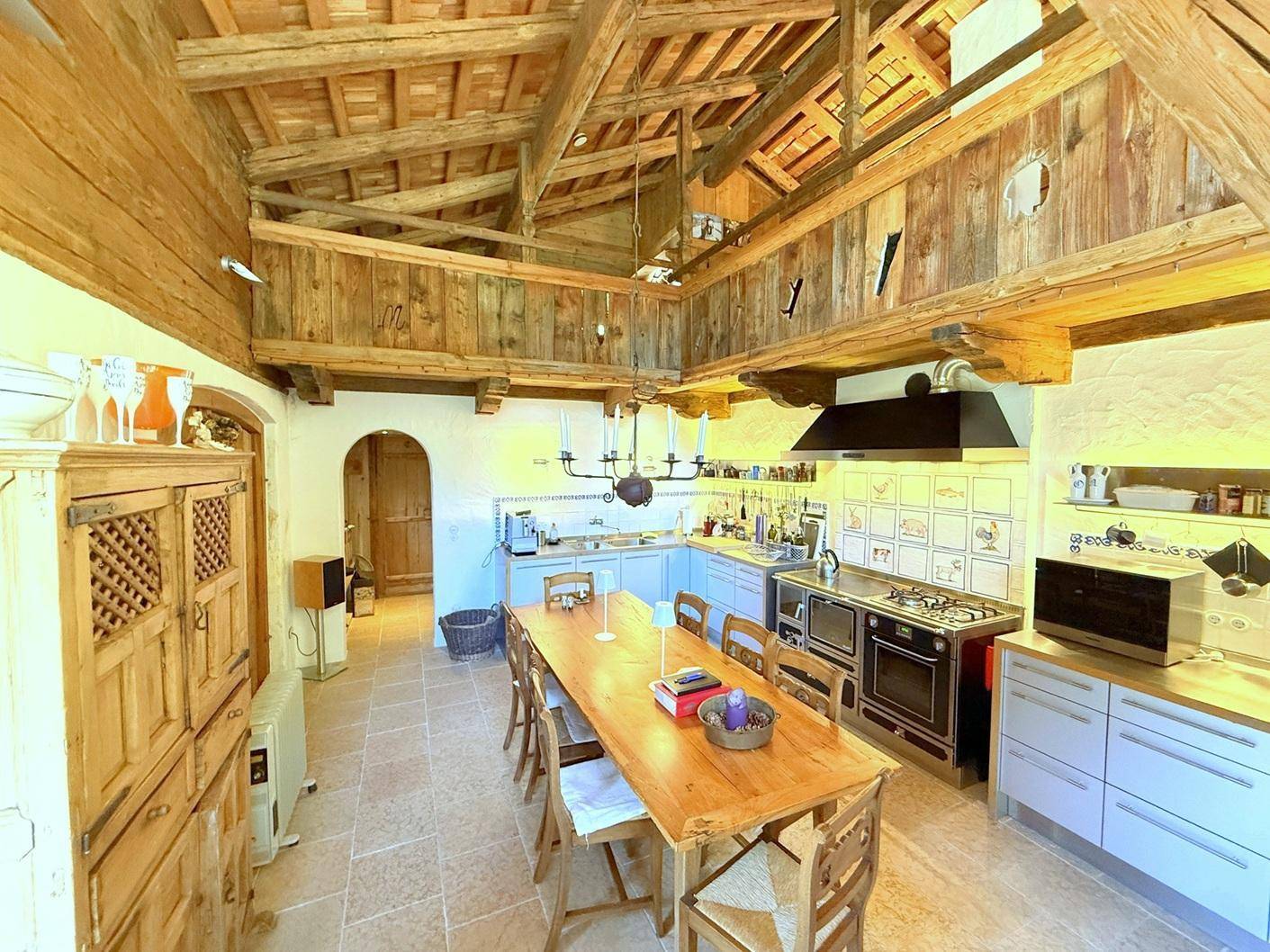 Rustikale Küche mit Holzbalken, großem Esstisch und traditionellem Herd in alpiner Atmosphäre.