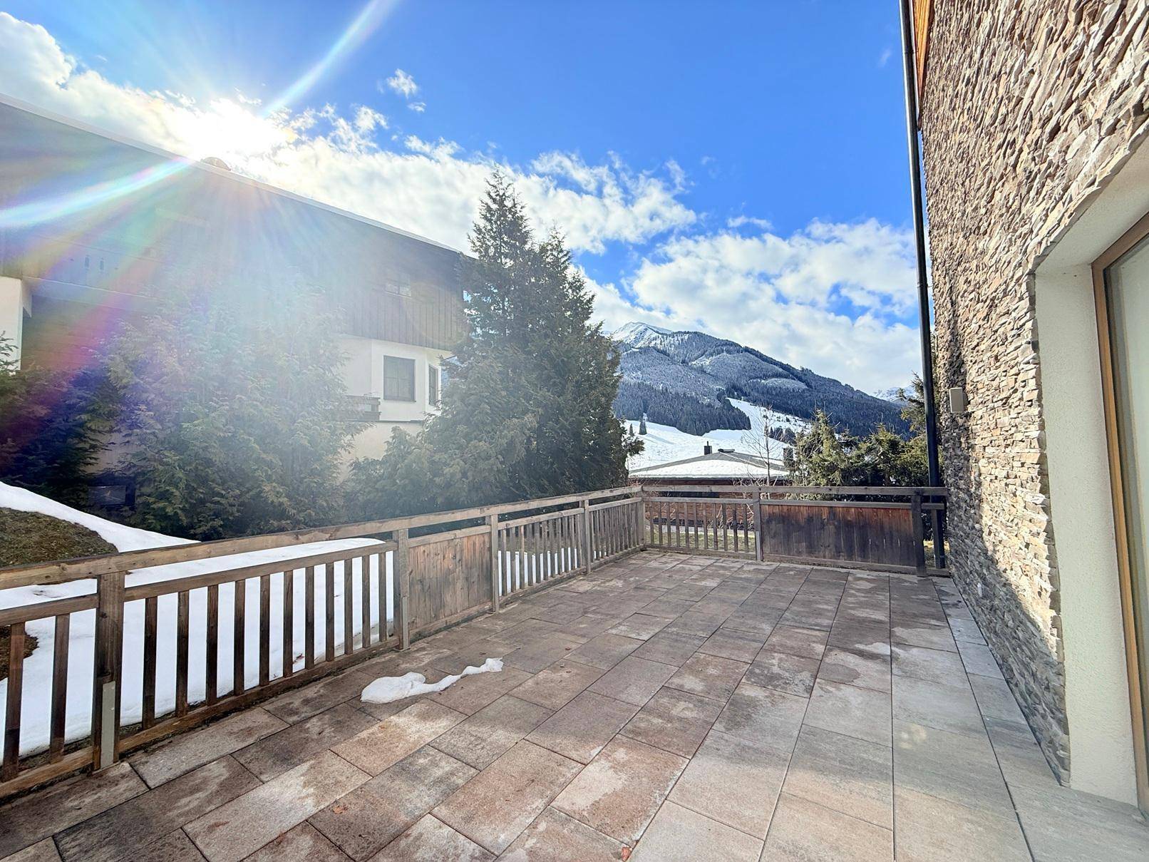 Geräumige, geflieste Terrasse mit Holzzaun und weitem Blick auf die schneebedeckten Berge.