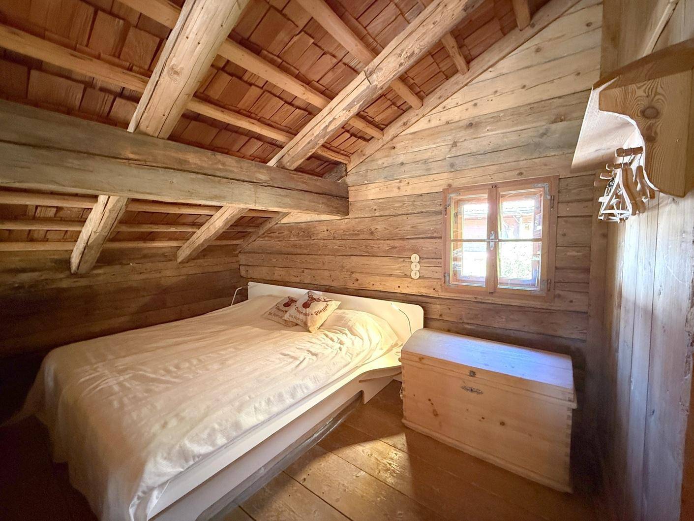 Rustikales Schlafzimmer im Dachgeschoss mit Holzwänden, Holzboden und sichtbaren Dachbalken.