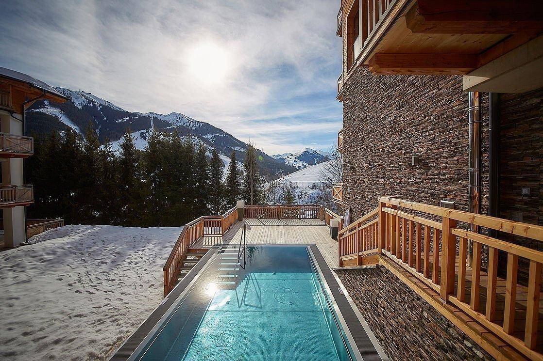 Außenpool mit Holzdeck und spektakulärem Blick auf die verschneiten Berge.