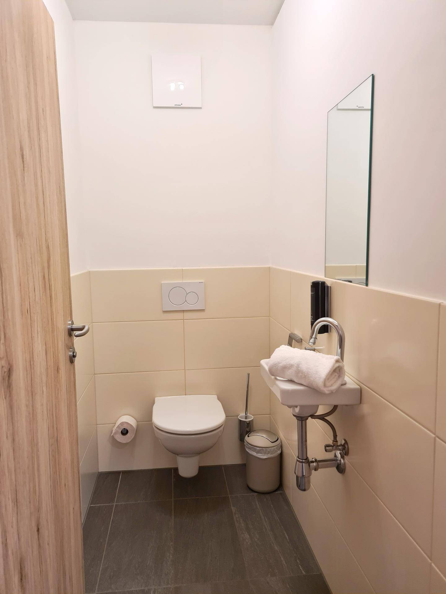 Kleines Gäste-WC mit Wand-WC, Waschbecken und hellen Fliesen.