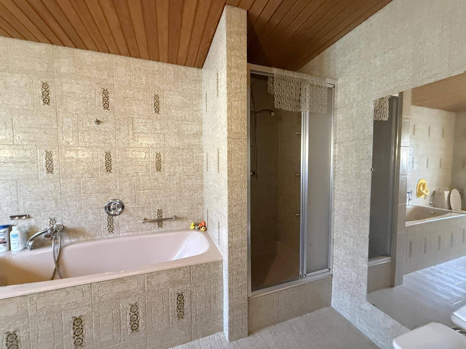 Badezimmer im Stil der 80er Jahre mit rosa Badewanne, Duschkabine und Holzdecke.