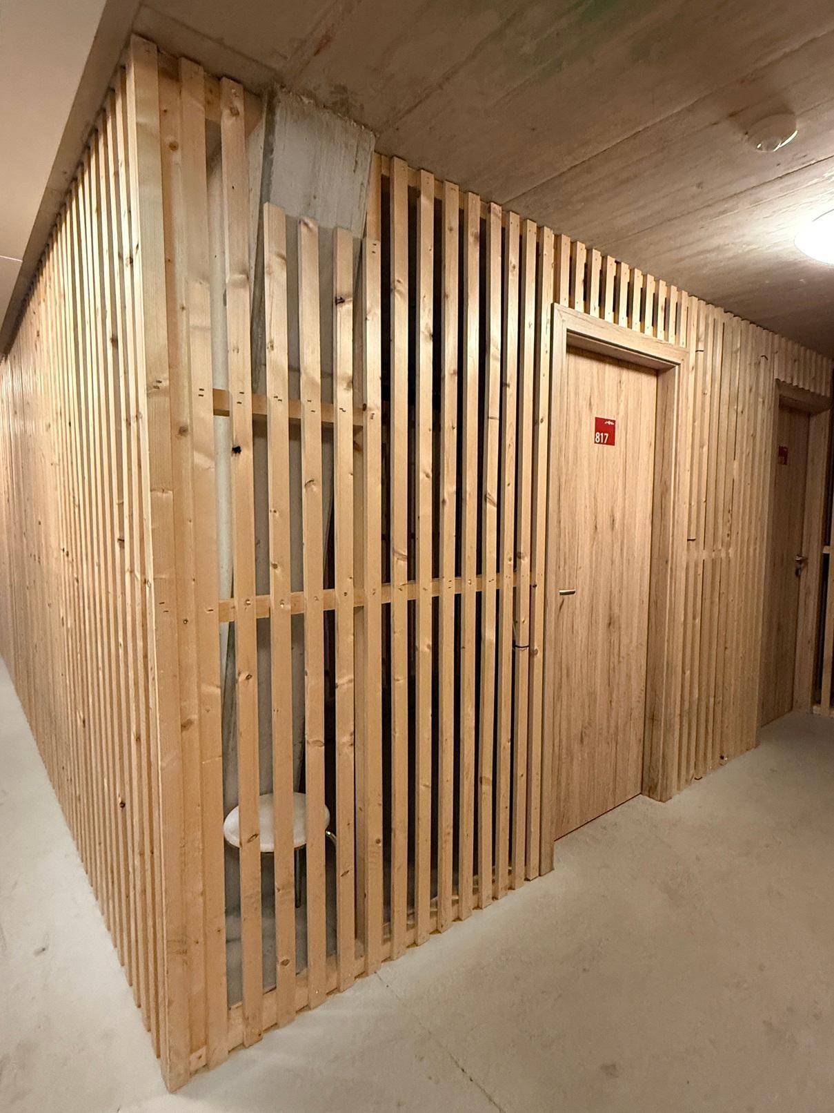 Moderner Flur mit Holzlamellenwänden und Betonboden, der zu den Lagerräumen führt.