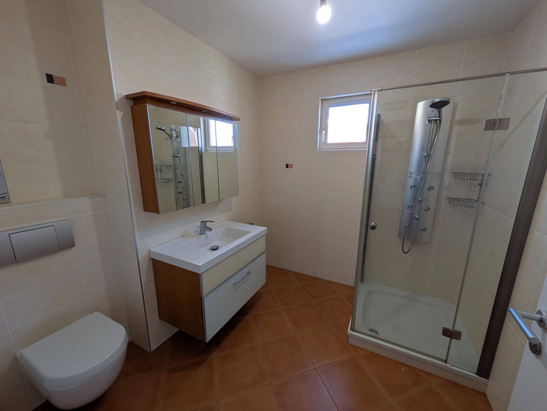 Modernes Badezimmer mit beigen Fliesen, Einzelwaschbecken, wandhängendem WC und großer Duschkabine.