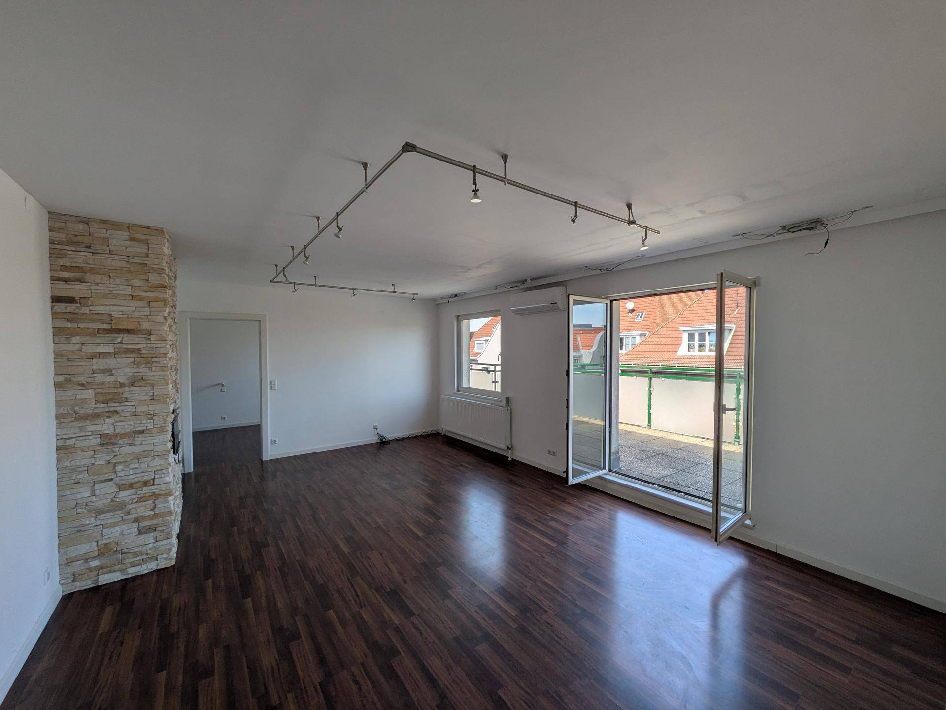 Helles Wohnzimmer mit dunklem Holzboden, einer Steinwand und Zugang zu einer großen Terrasse.