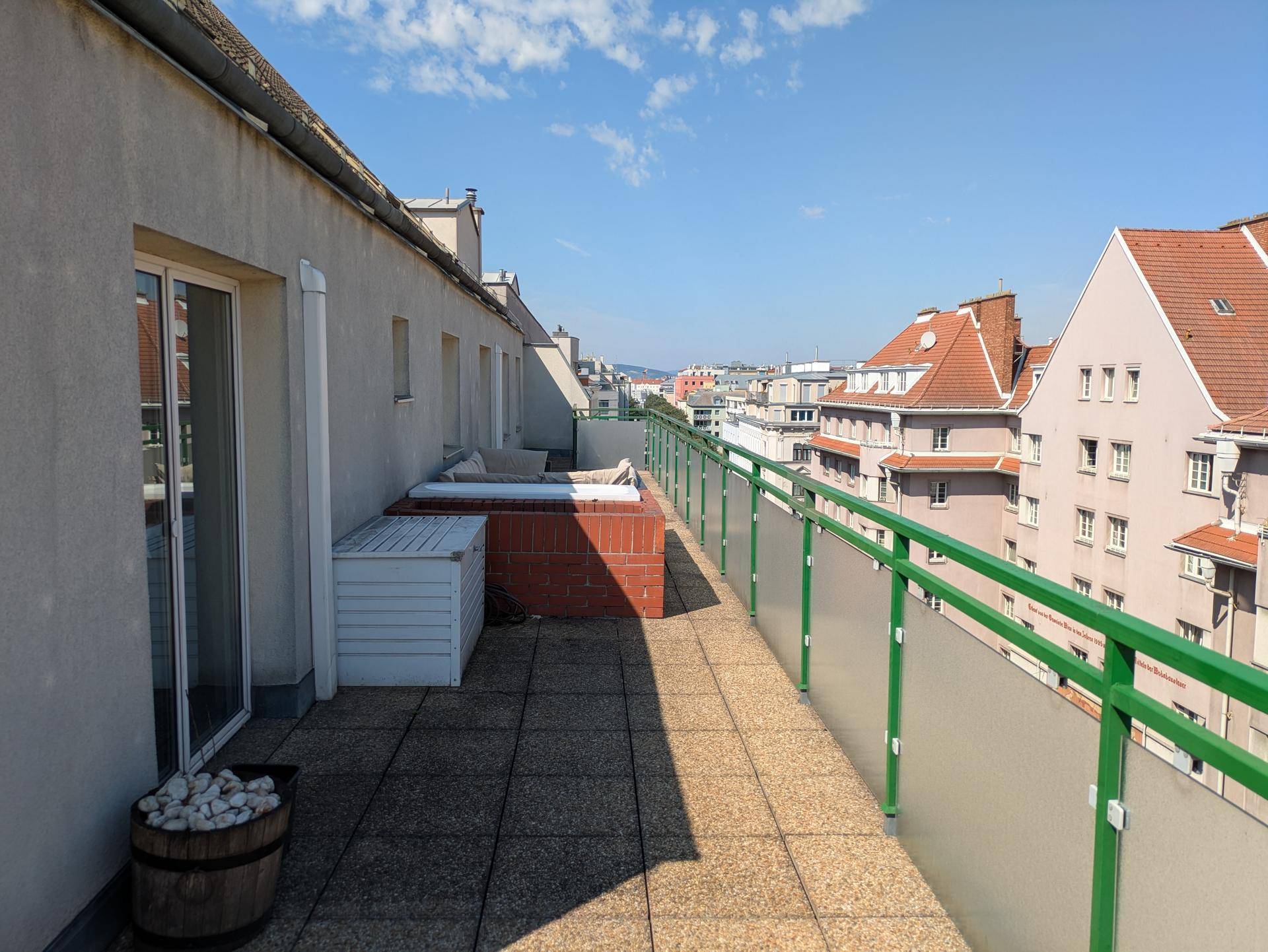 Sonnige Dachterrasse mit Fliesenboden, grünem Geländer und einem Whirlpool, bietet einen weiten Stadtblick.