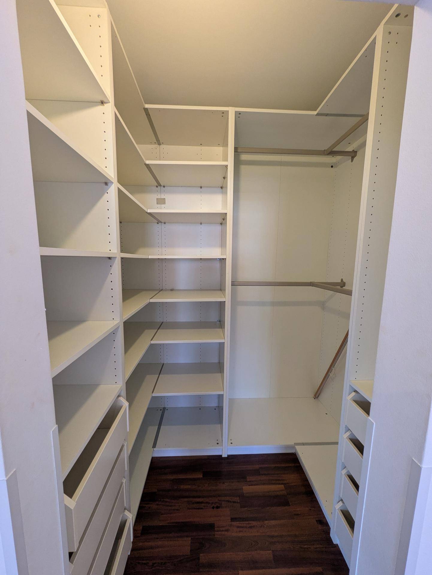 Begehbarer Kleiderschrank mit weißen Regalen, Schubladen und viel Stauraum für Kleidung.