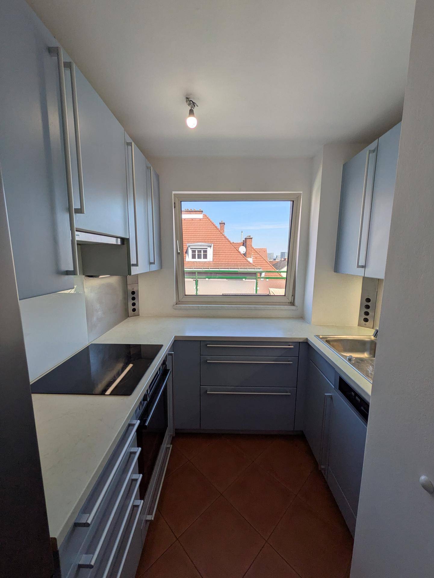 Moderne, schmale Küche mit hellgrauen Schränken, Induktionskochfeld und Fensterblick über die Dächer.