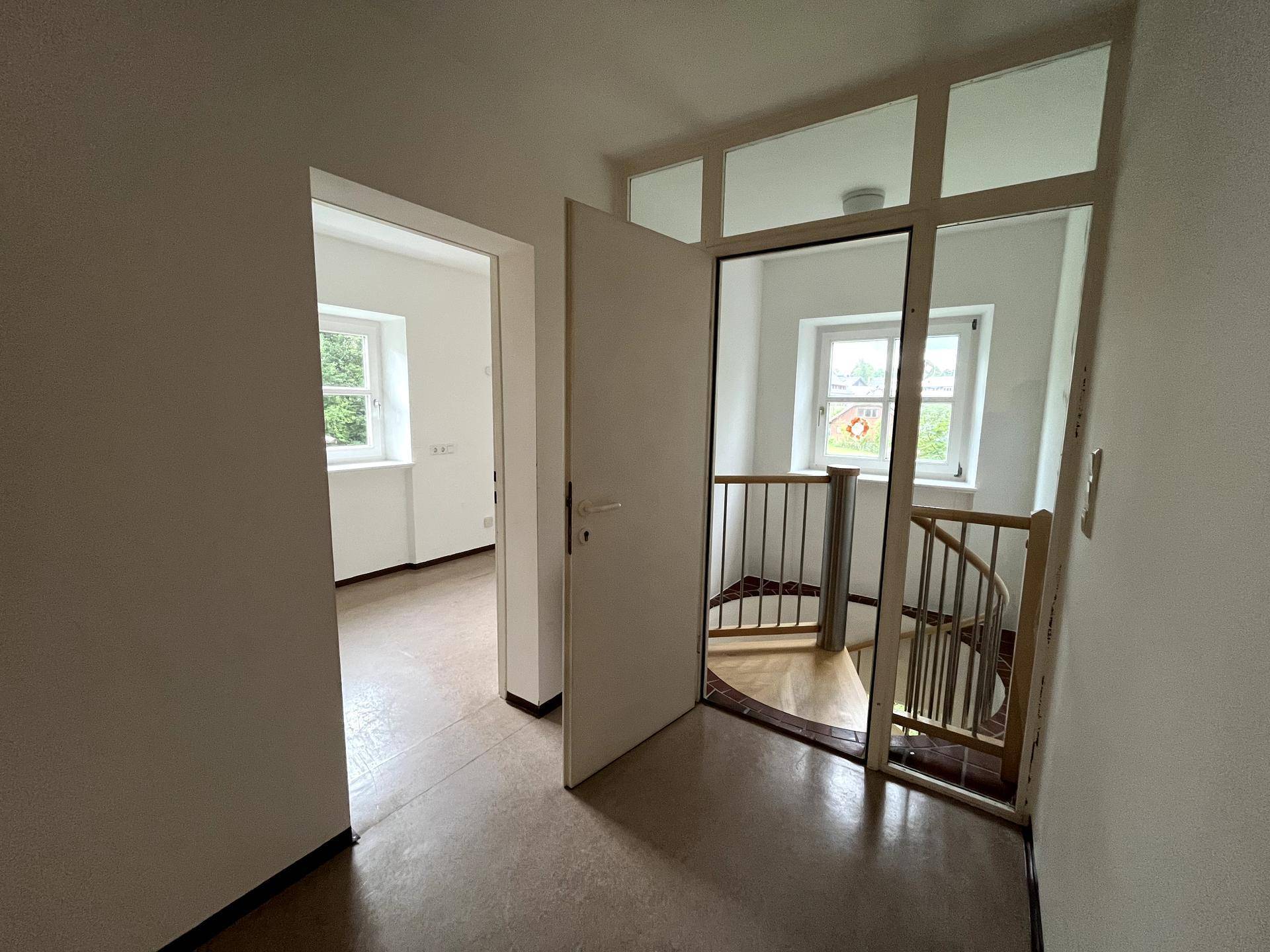 Heller Flur mit Zugang zu weiteren Räumen und einer Holztreppe ins obere Stockwerk.