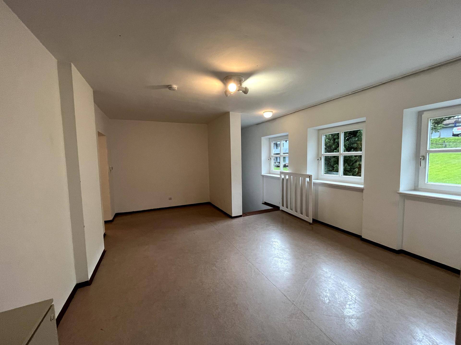 Geräumiges, leeres Zimmer mit mehreren Fenstern, Linoleumboden und Heizkörper.