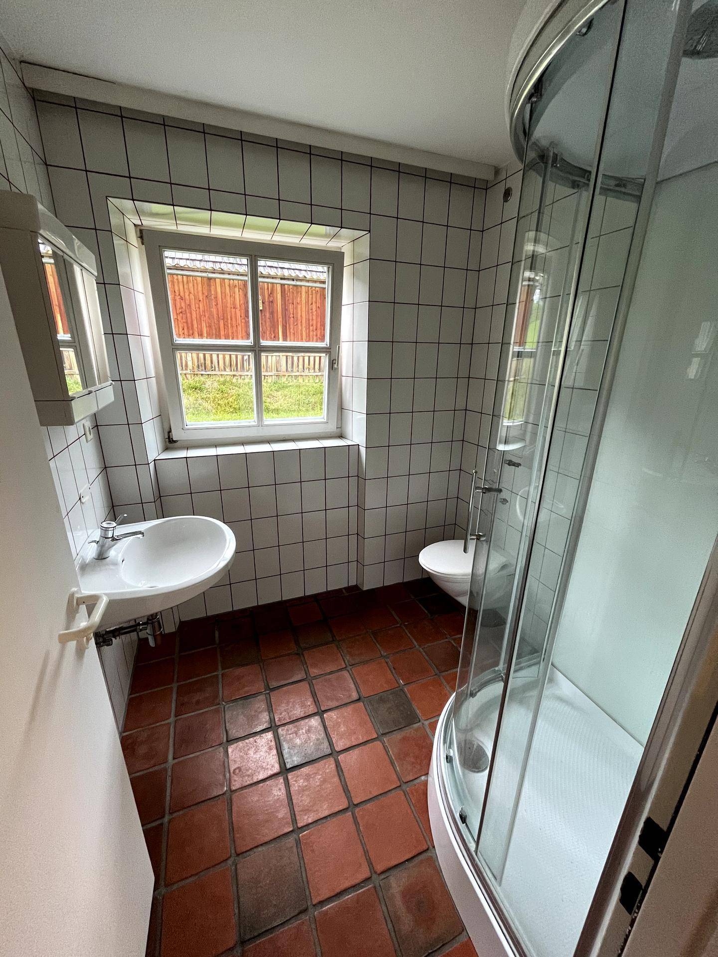 Funktionales Badezimmer mit Duschkabine, WC, Waschbecken und Fenster, komplett gefliest.