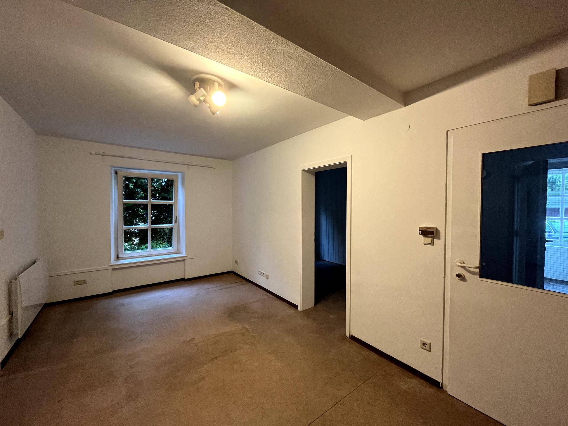 Helles Zimmer mit einem Fenster und Blick ins Grüne, bereit zur individuellen Gestaltung.