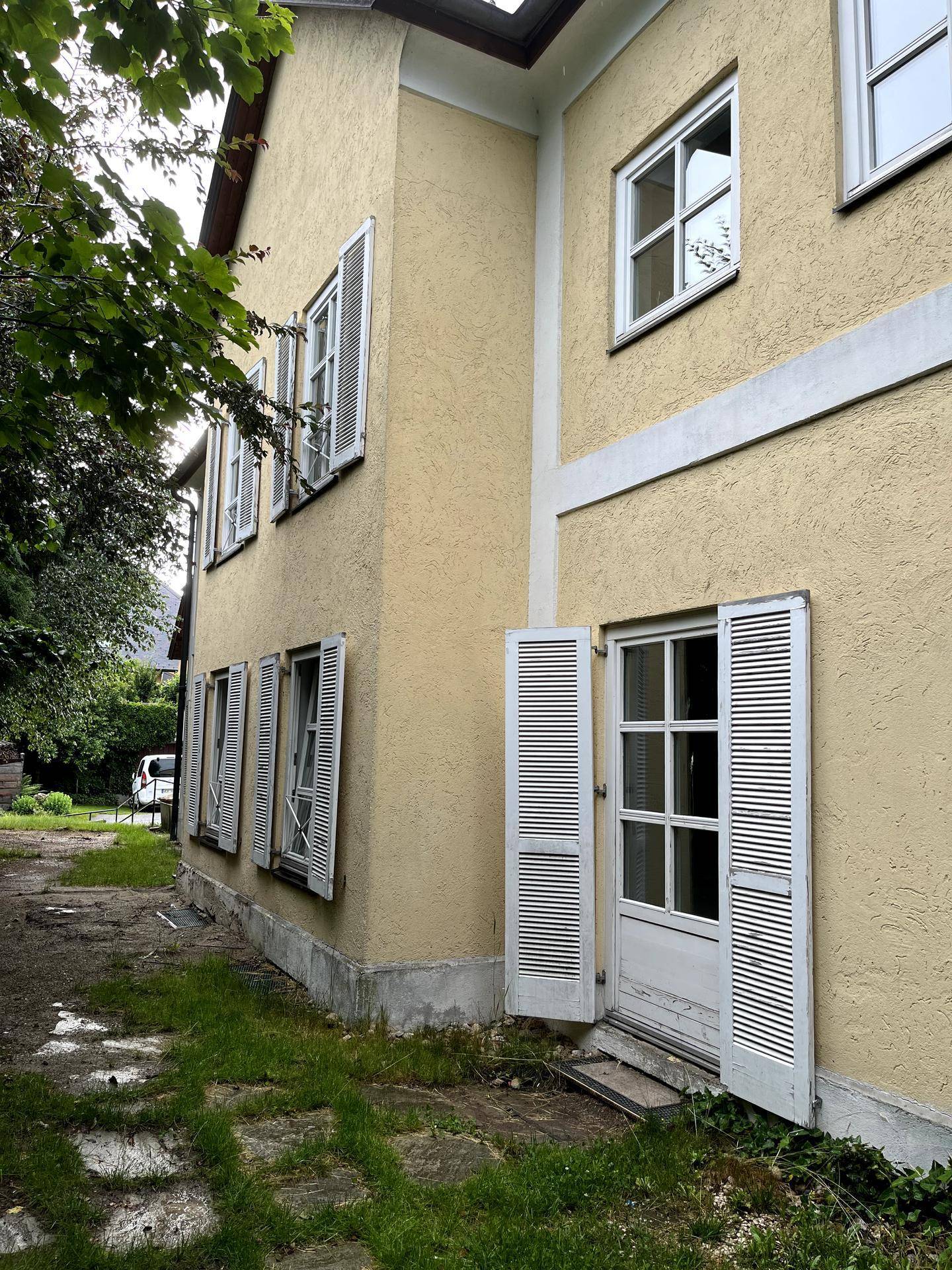 Seitenansicht des gelben Gebäudes mit mehreren Fenstern und geöffneten Fensterläden.