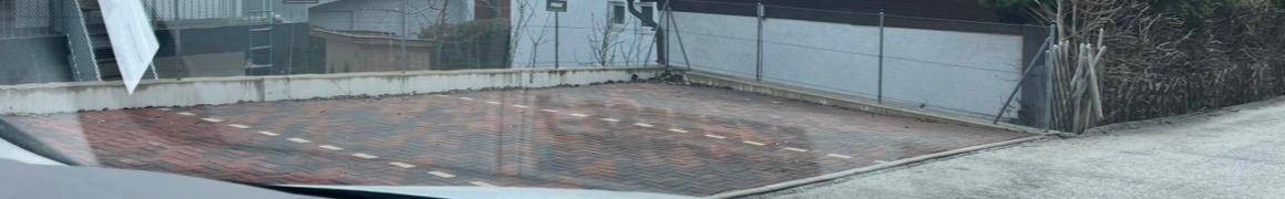 Übersicht über einen gepflasterten Parkplatz mit Ziegelsteinen und weißen Markierungen, umgeben von einer niedrigen Mauer.