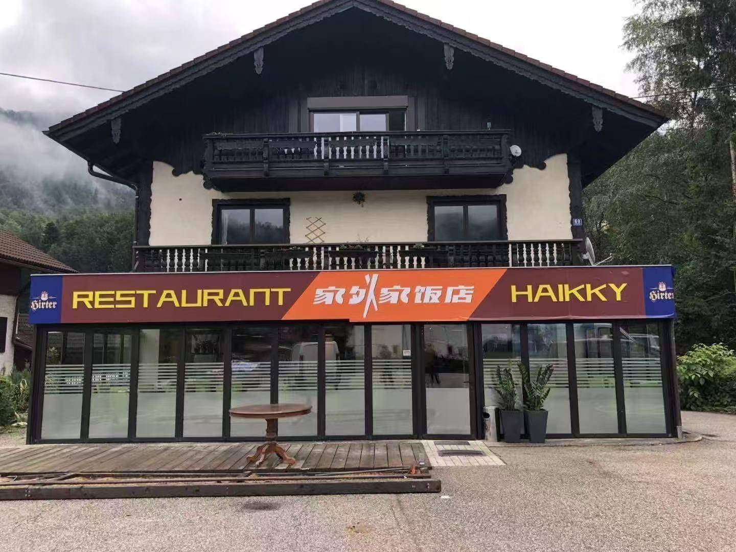 Traditionelles Gebäude mit Restaurantfassade, großen Fenstern und Balkonen im Obergeschoss.