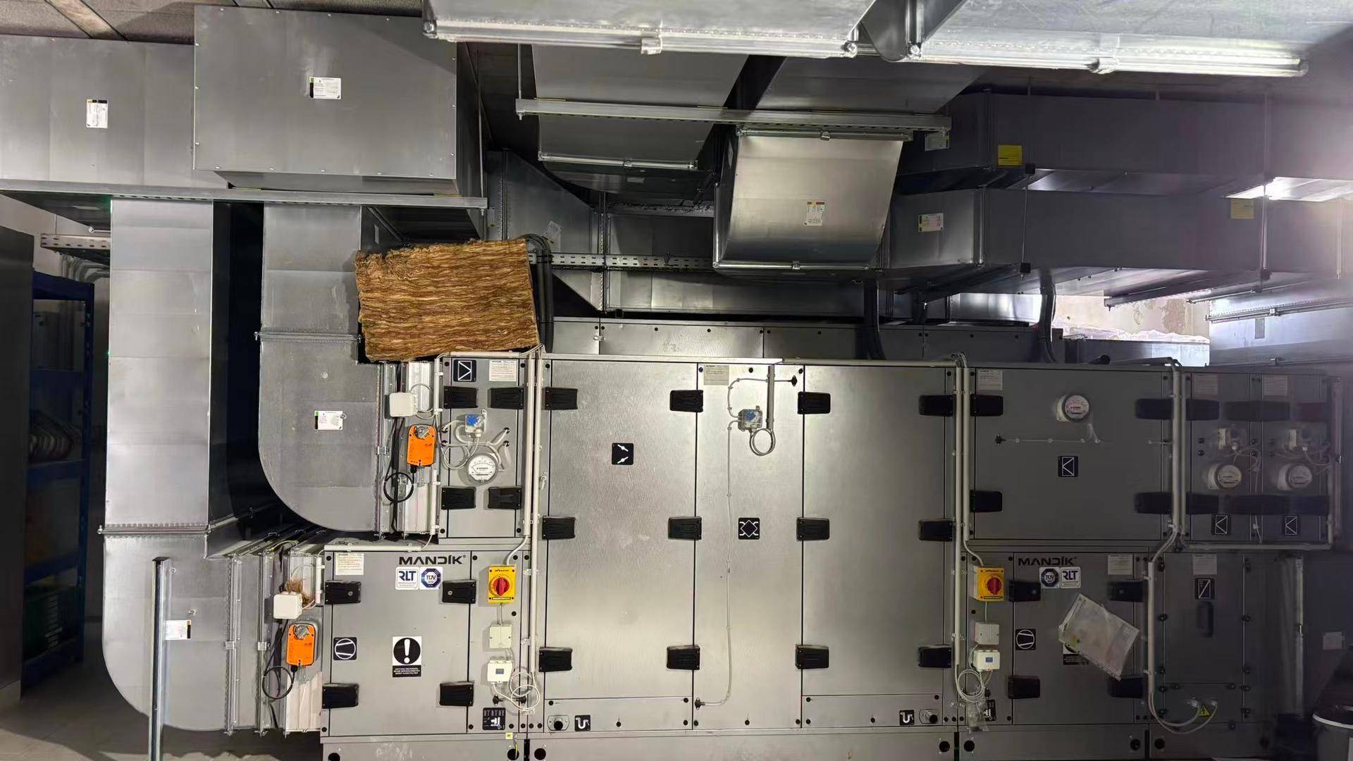 Technikraum mit umfangreicher Lüftungsanlage und großen Metallrohren an der Decke.