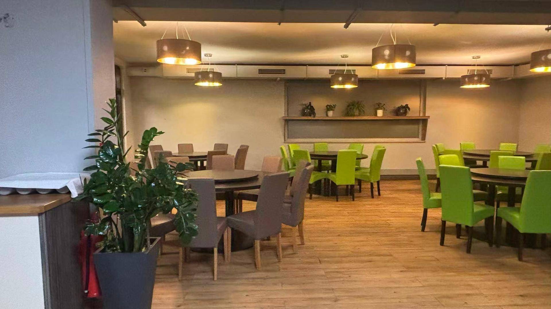 Gemütlicher Restaurantraum mit indirekter Beleuchtung, Holzboden und runden Tischen.
