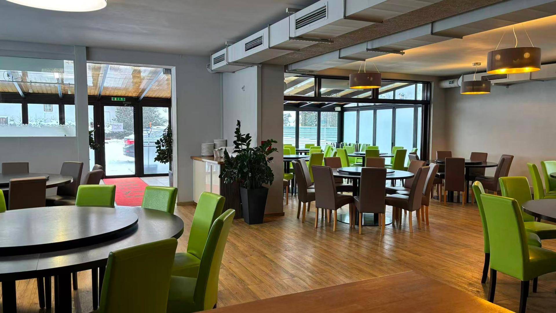 Geräumiger Restaurantbereich mit Holzboden, runden Tischen und vielen grünen Stühlen.