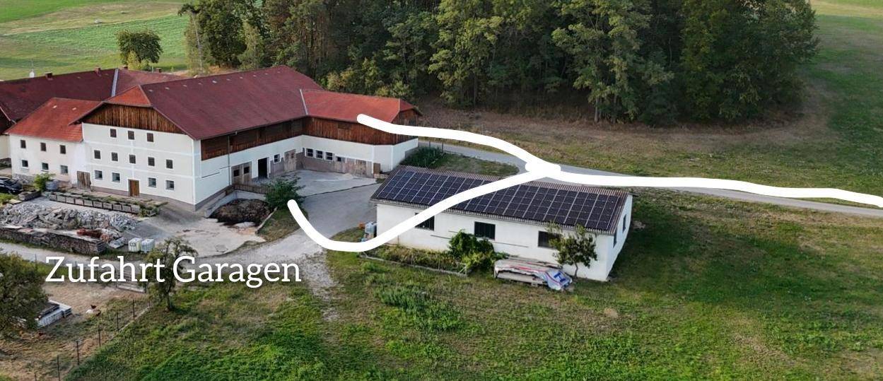 Luftaufnahme des Anwesens mit mehreren Gebäuden, umgeben von grünen Feldern und Wäldern, mit Zufahrtsweg.