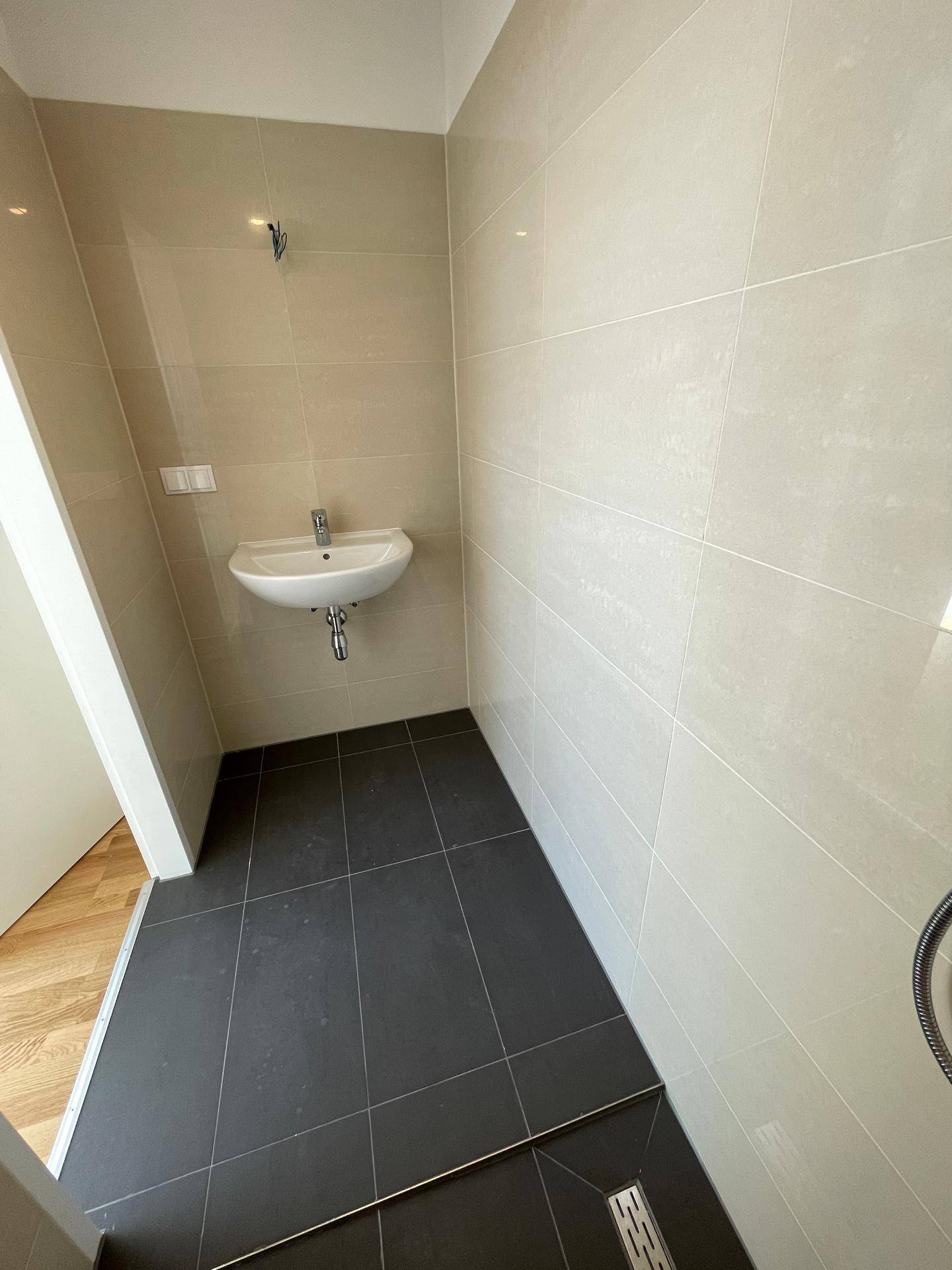 Modernes Badezimmer mit beigen Wandfliesen, dunklem Boden und einem Waschbecken.