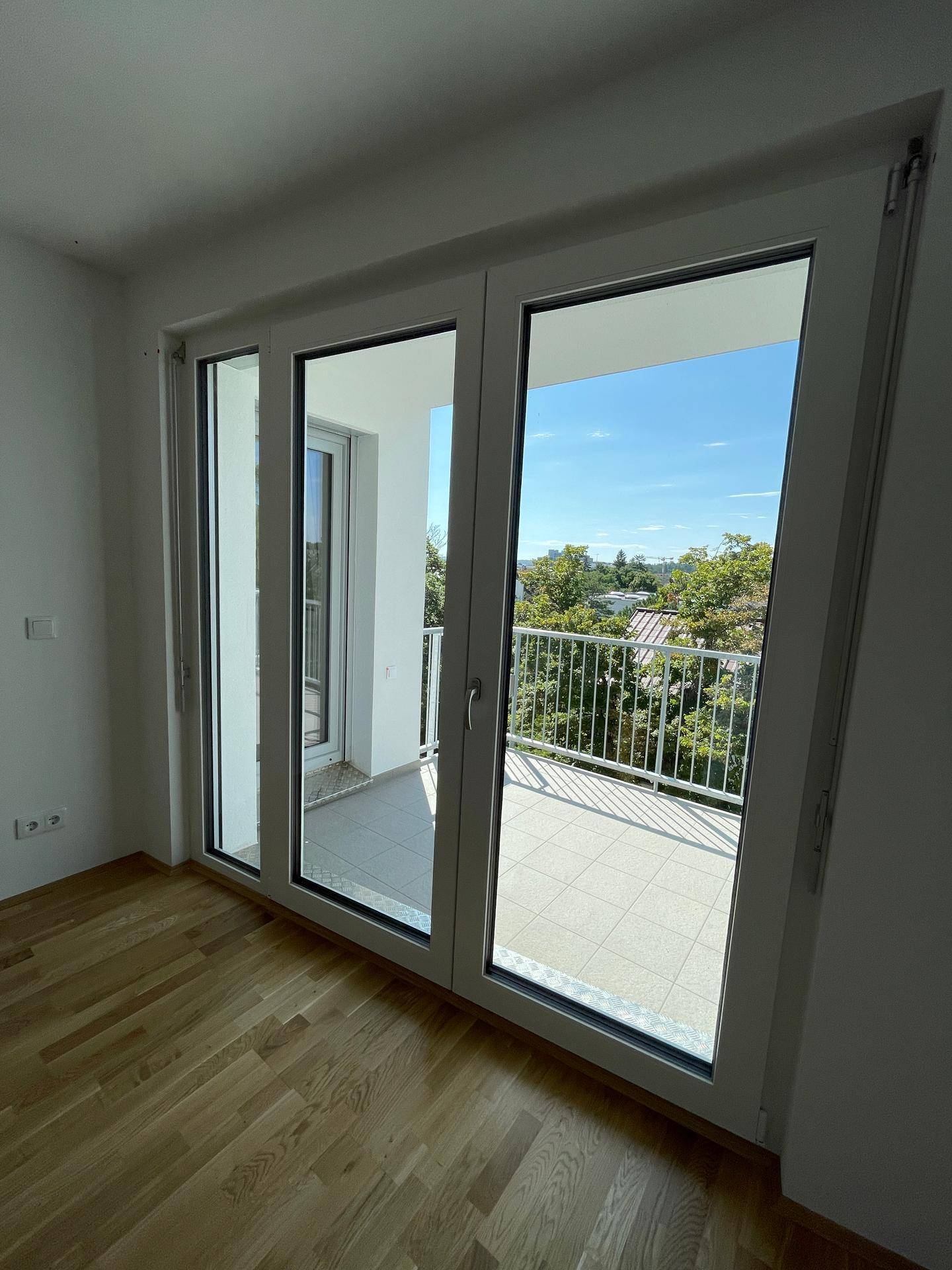 Heller Raum mit Parkettboden und großem Fenster, das Zugang zu einem Balkon bietet.
