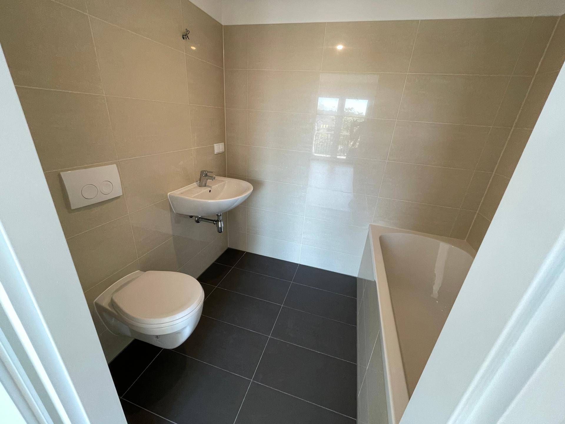 Modernes Badezimmer mit Badewanne, Toilette und Waschbecken, hell gefliest.