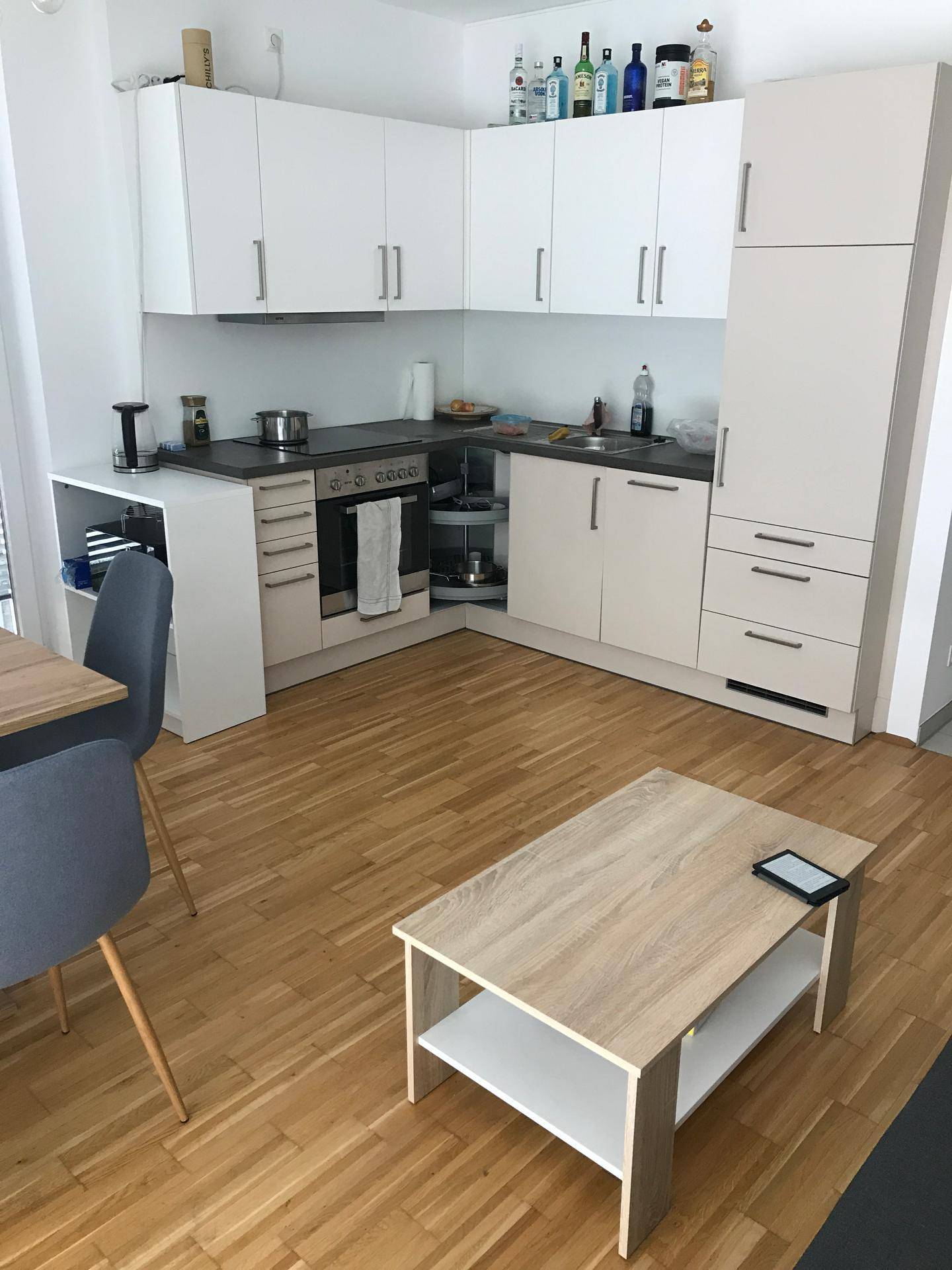 Moderne Einbauküche mit weißen Schränken, Kochfeld und Holzboden in offenem Bereich.