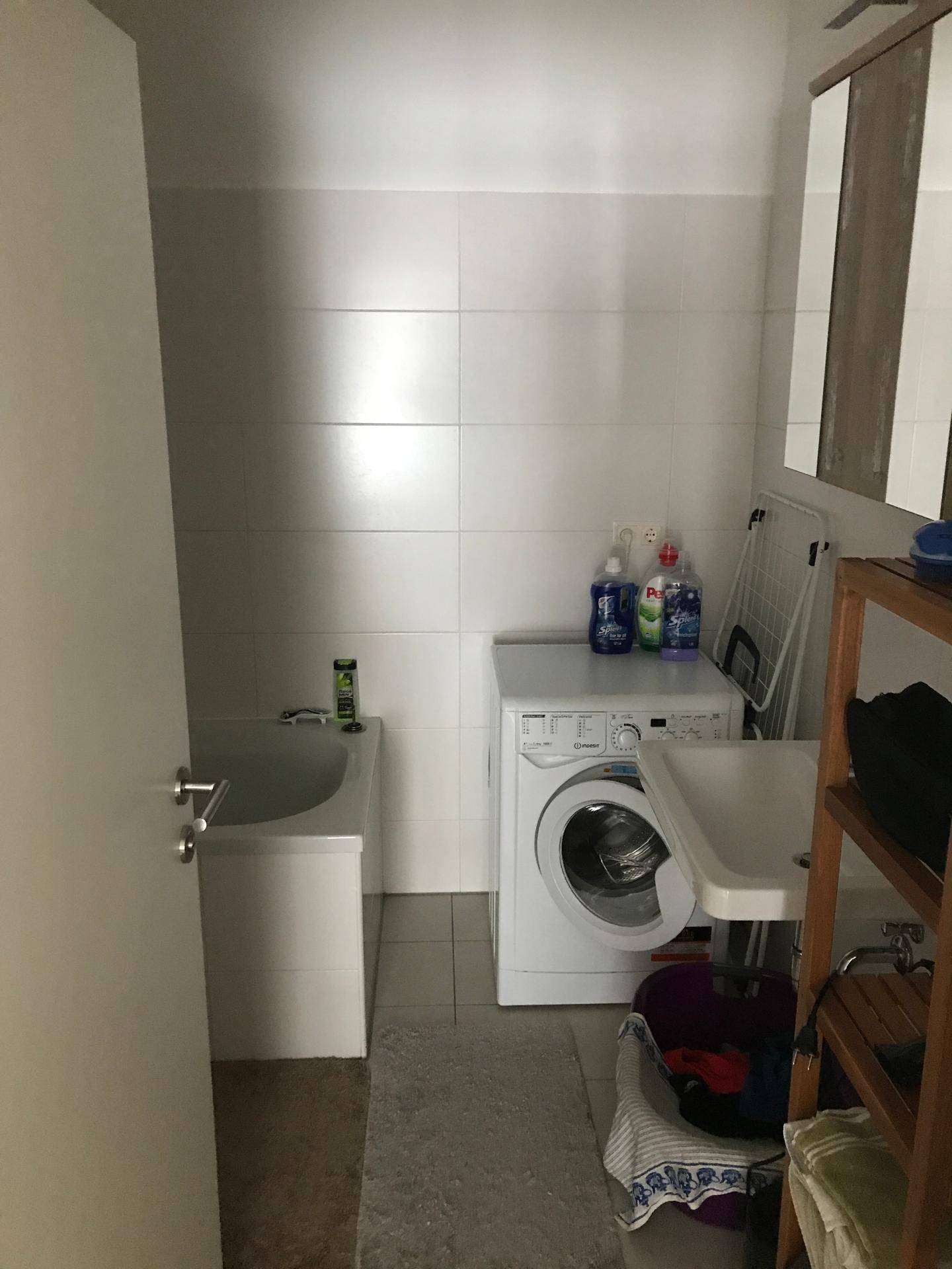 Funktionales Badezimmer mit Badewanne, Waschmaschine und weißen Fliesen.