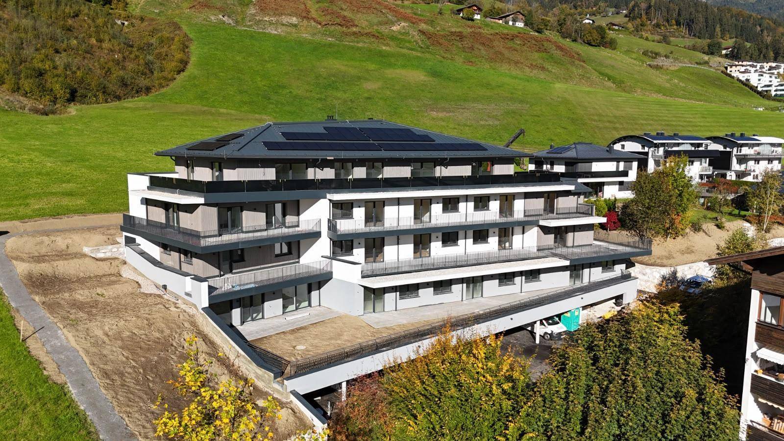 Luftaufnahme eines modernen Apartmentgebäudes mit Photovoltaikanlage auf dem Dach und grüner Umgebung.