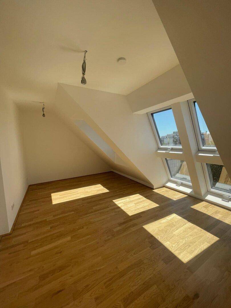 Lichtdurchfluteter Raum im Dachgeschoss mit Holzboden und mehreren Dachfenstern, die eine helle Atmosphäre schaffen.