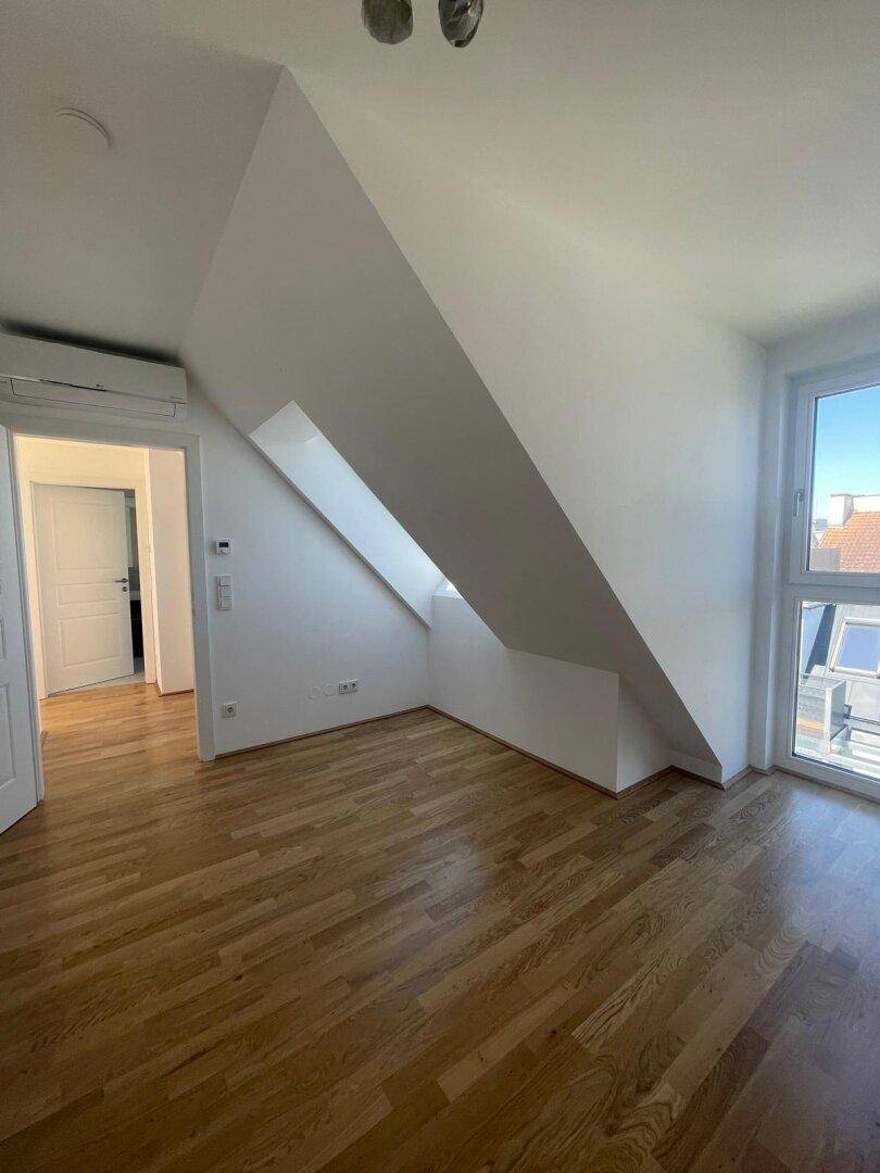 Helles Dachgeschosszimmer mit Holzboden, Klimaanlage und Zugang zu weiteren Räumen.