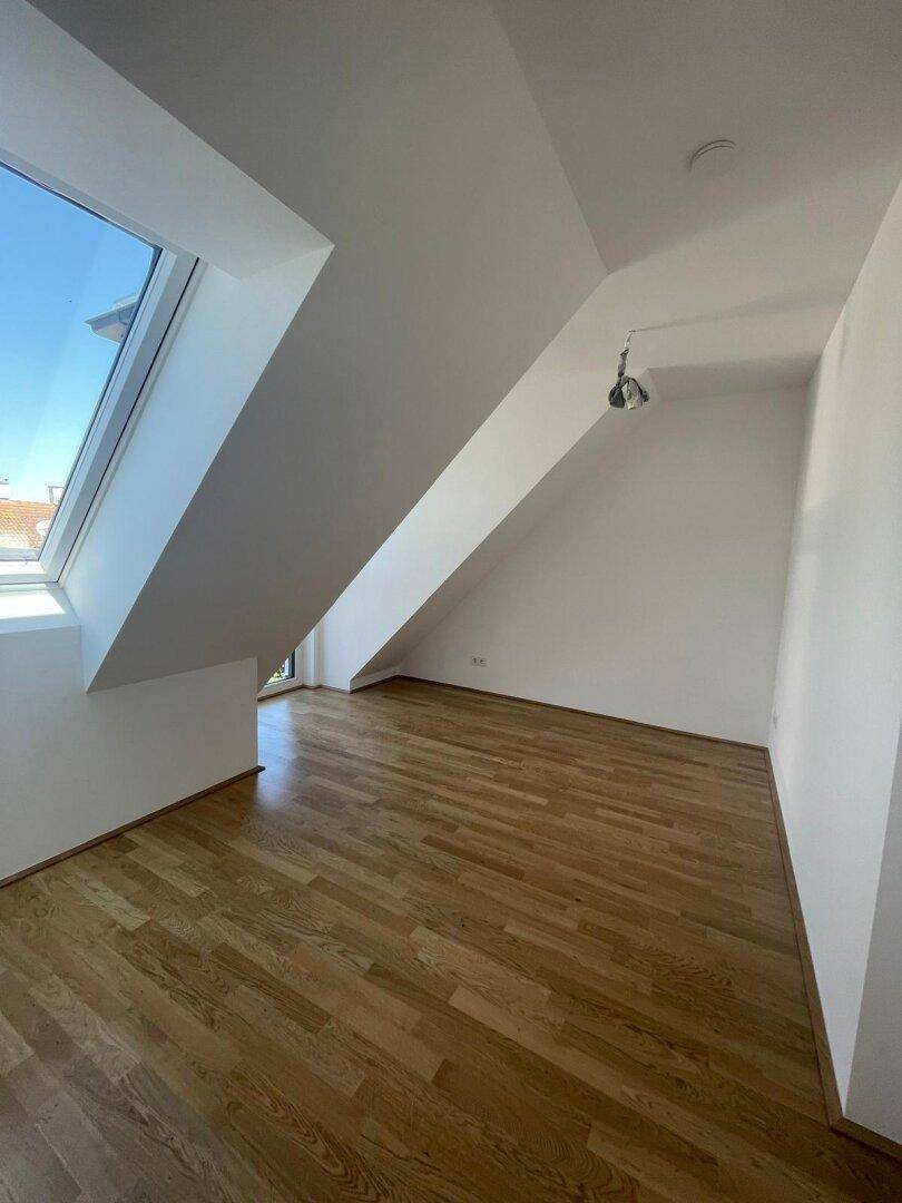 Sonniger Dachgeschossraum mit Holzboden und einem großen Dachfenster, das eine angenehme Wohnatmosphäre schafft.