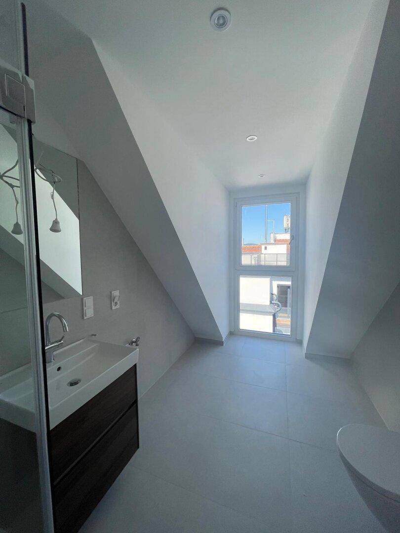 Helles Badezimmer mit modernem Waschtisch, Dusche und Fenster, das viel Tageslicht hereinlässt.