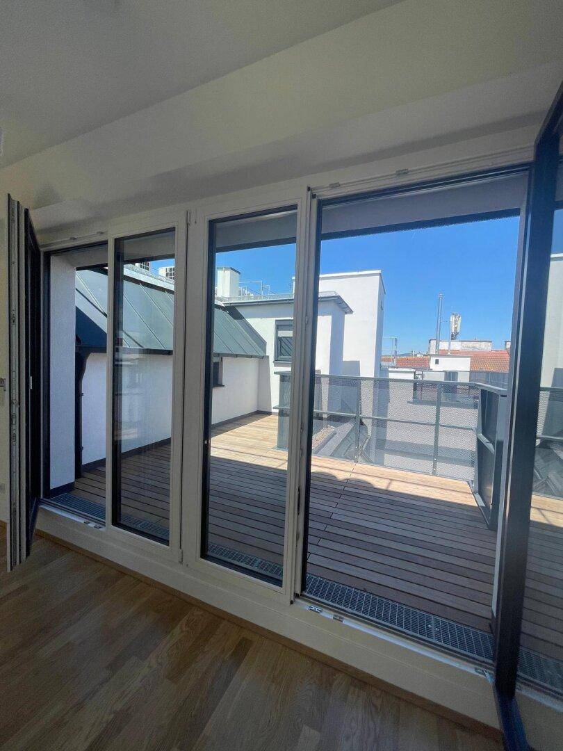 Heller Wohnbereich mit großen Fenstern und direktem Zugang zur Dachterrasse, die einen weiten Blick bietet.