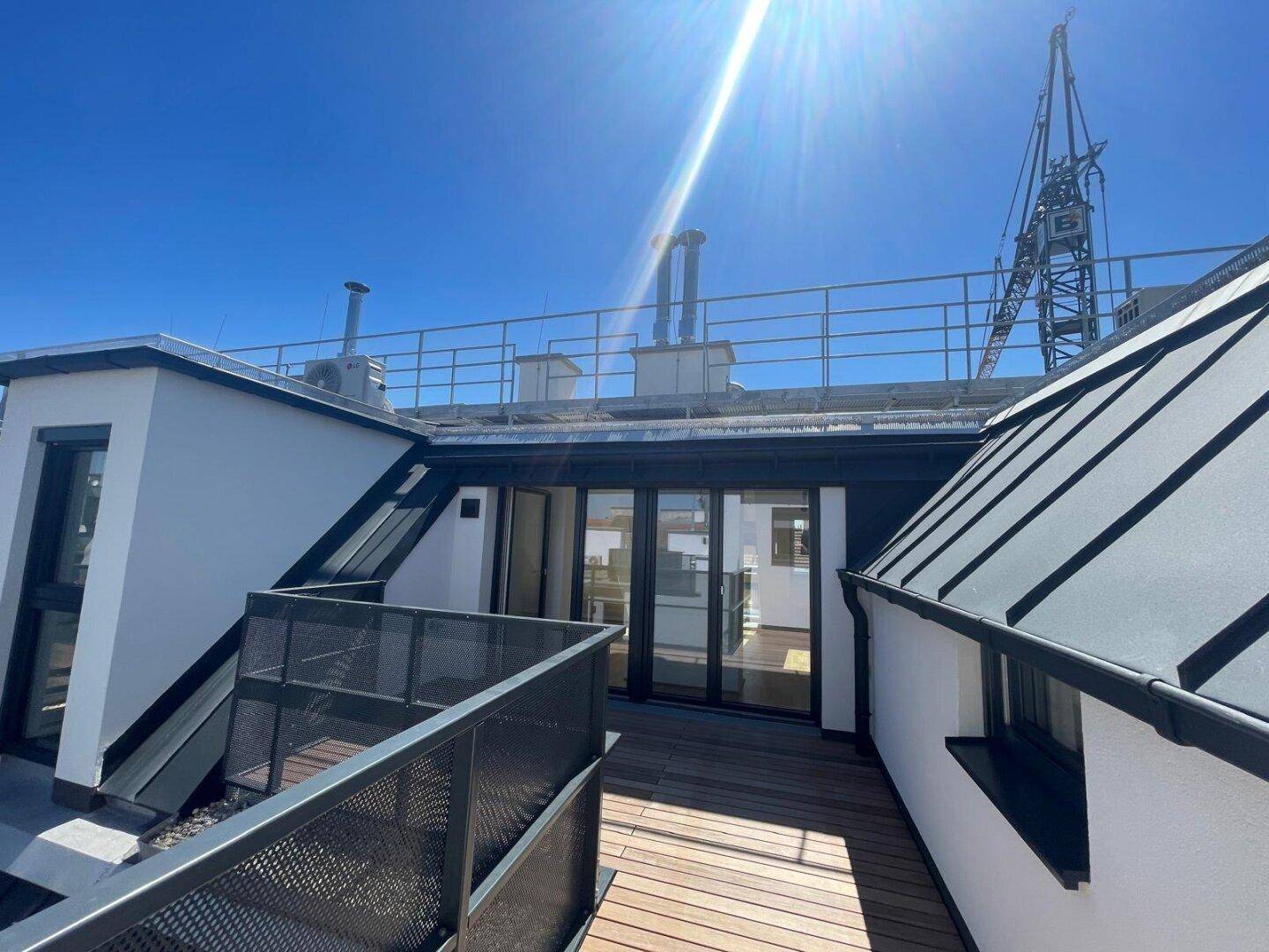Weitläufige Dachterrasse mit Holzboden und Blick auf die umliegenden Gebäude und den blauen Himmel.