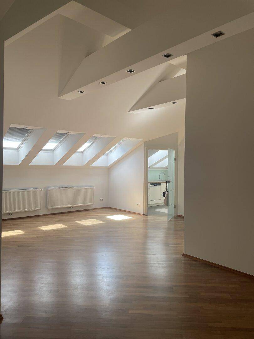 Lichtdurchfluteter Wohnbereich im Dachgeschoss mit Holzboden und Blick in die Küche.