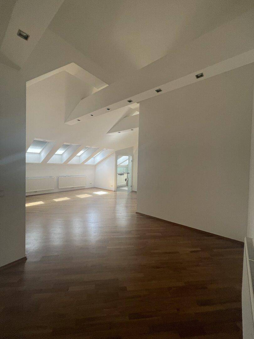 Geräumiges Dachgeschoss-Wohnzimmer mit Holzboden und schrägen Wänden, ideal für offenes Wohnen.