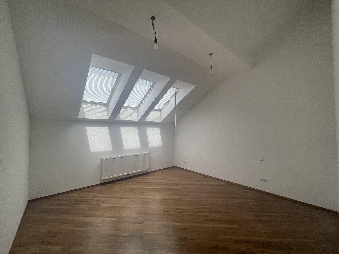 Geräumiges Dachgeschosszimmer mit Holzboden und mehreren Dachfenstern für viel Tageslicht.
