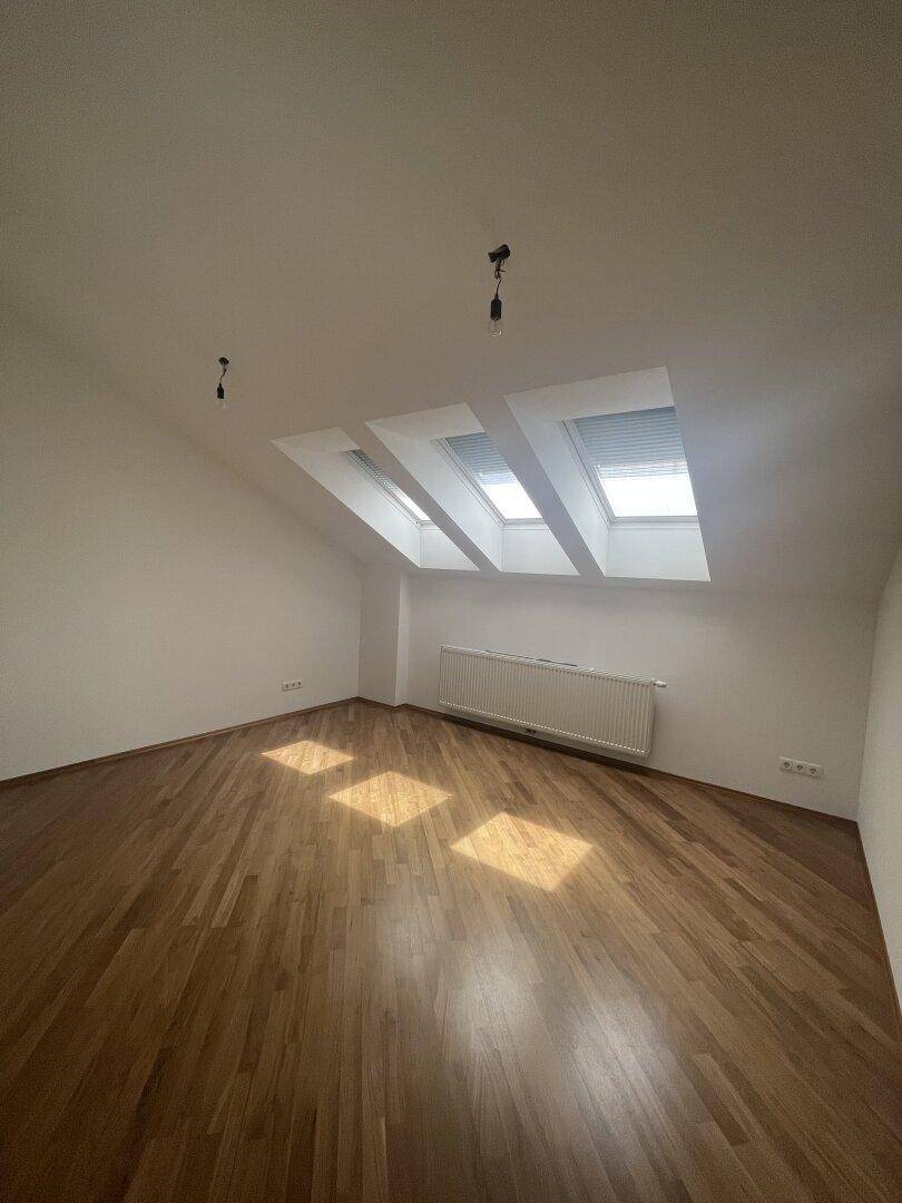 Dachgeschosszimmer mit Holzboden und drei Dachfenstern, die viel Sonnenlicht hereinlassen.