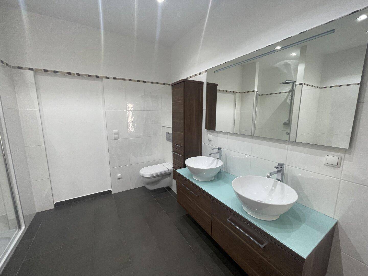 Geräumiges Badezimmer mit Doppelwaschbecken, Toilette und großem Spiegelschrank.