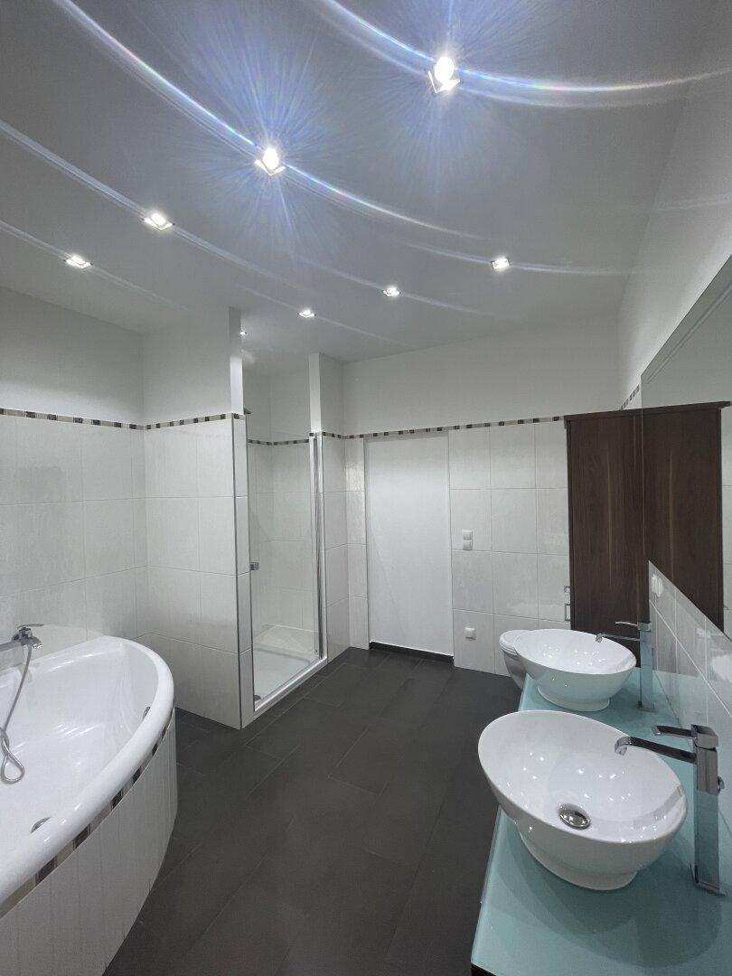 Helles Badezimmer mit moderner Beleuchtung, Eckbadewanne und Doppelwaschbecken.