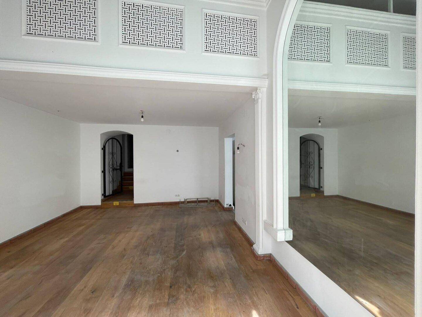 Geräumiger Ladenbereich mit Holzboden, hohen Decken und dekorativen Lüftungsgittern an der Wand.